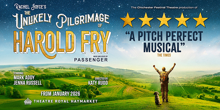 A man in a beige coat walks along a path surrounded by green grass and trees.