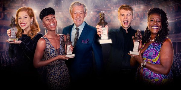Three people celebrate holding awards, smiling widely; a woman in a patterned dress, a man in a suit, and a young man in black.