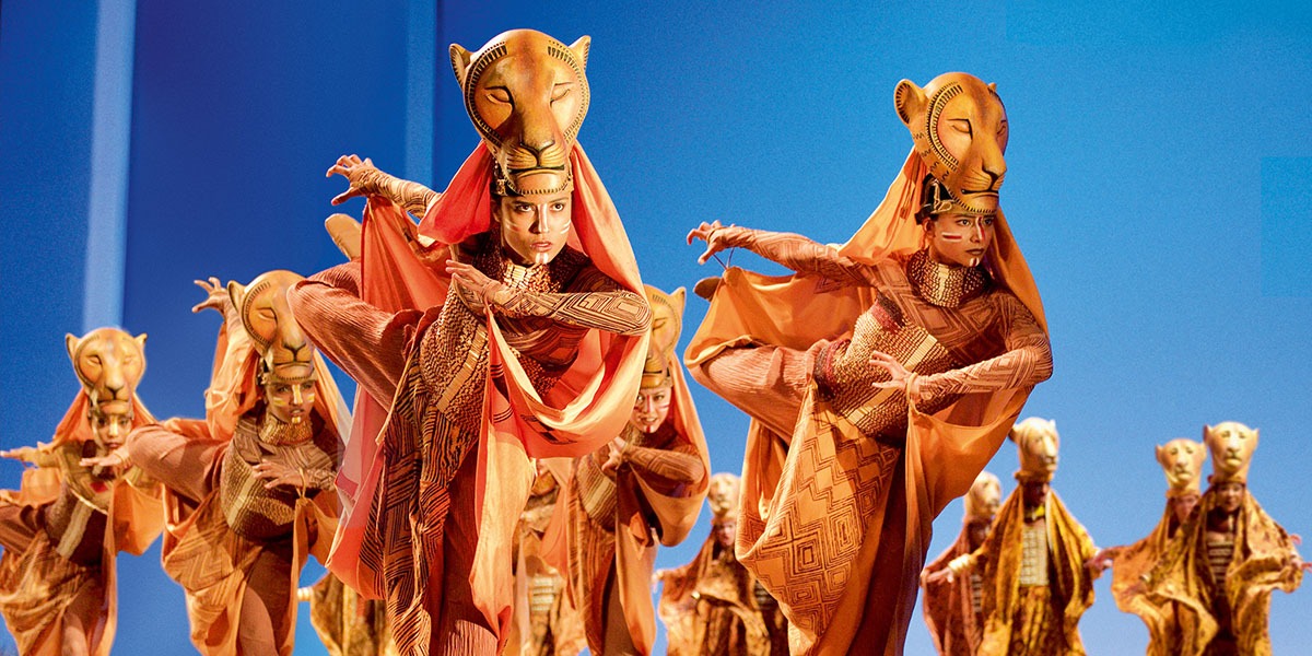 Performers in vibrant orange costumes with lion masks, striking dynamic poses against a blue background.