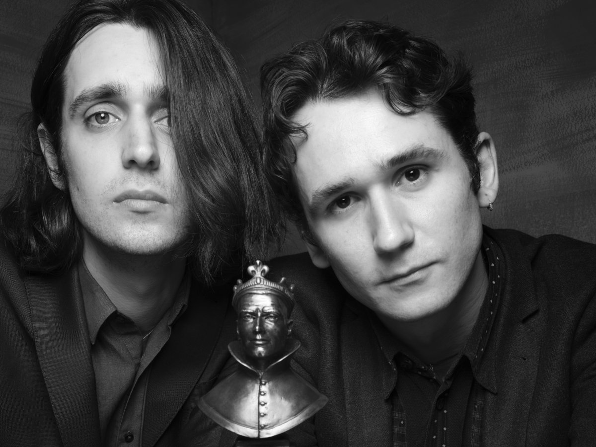 Two young men look into the camera. There is an Olivier Award between them.