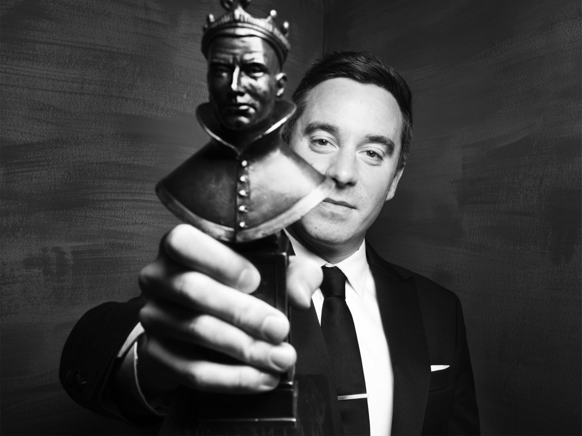 A person in a suit holds out award in front of them. Black and white image.