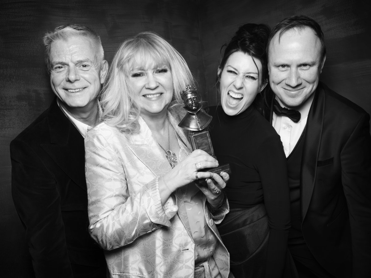 Two men and two women standing next to each other and smiling. The woman on the left is holding an Olivier Award statue in her hands.