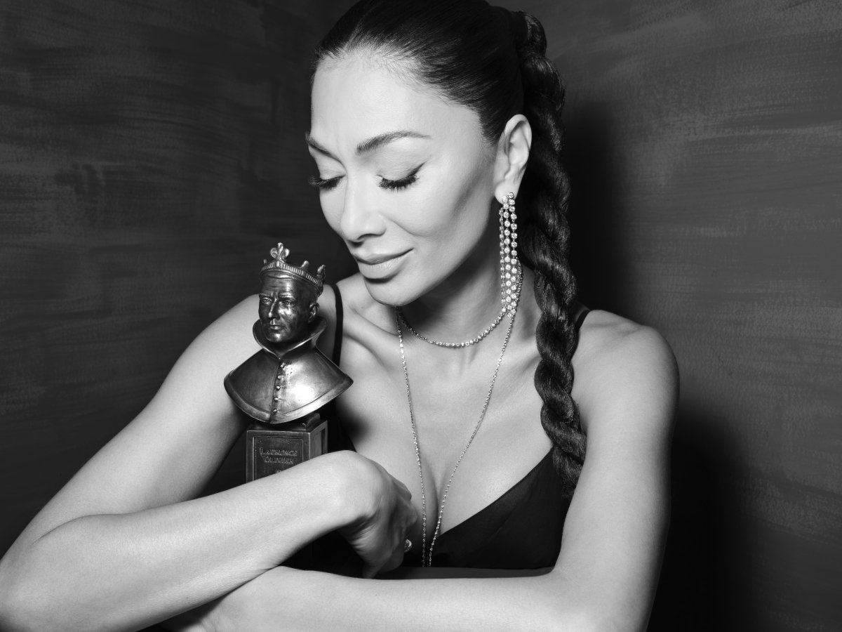 A woman with a long ponytail plait. She is embracing an Olivier Award statue. Her face is angled down towards the statue and she has a soft smile.