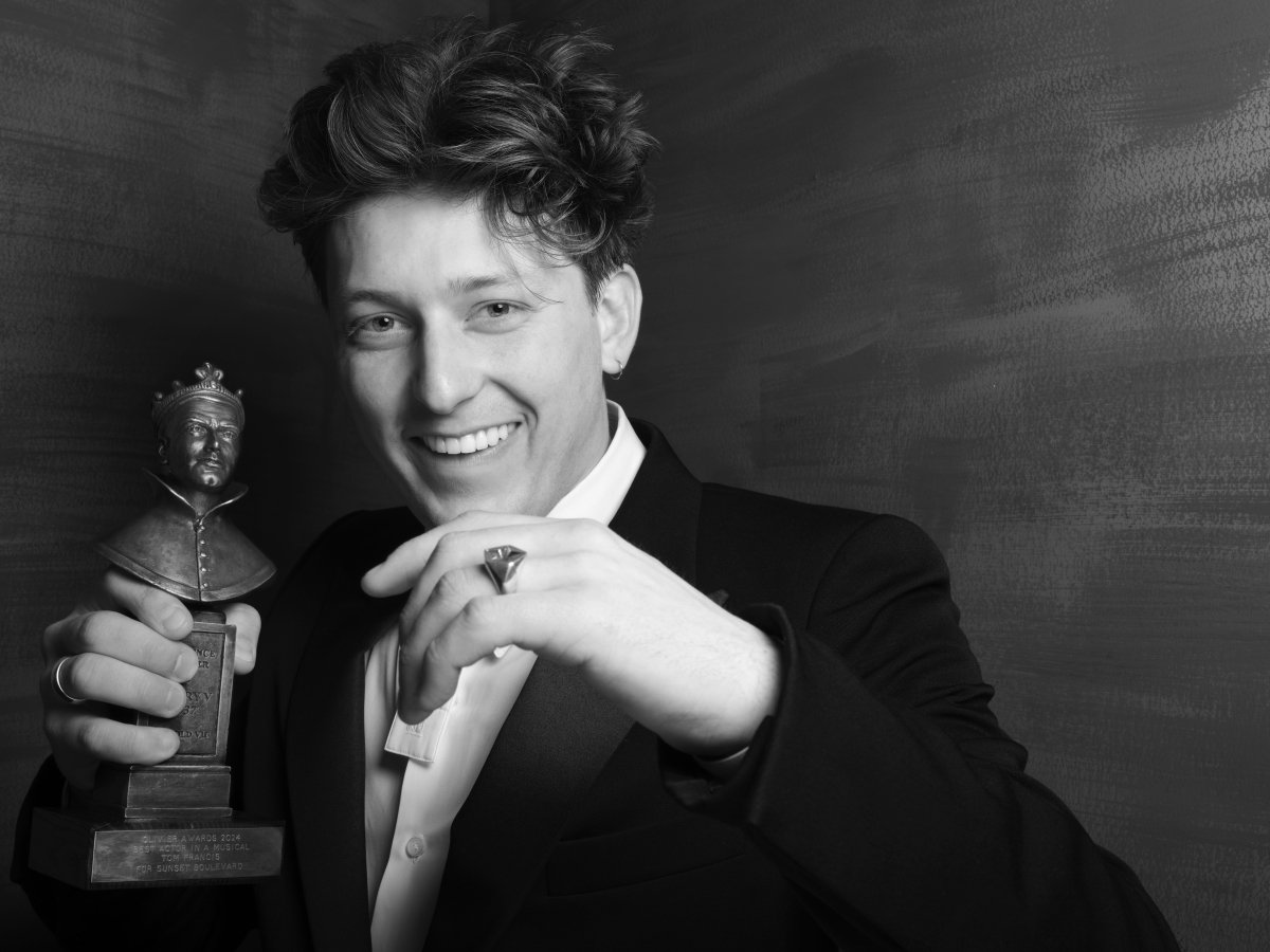 A person smiling to camera with their hand up. Holding an award.