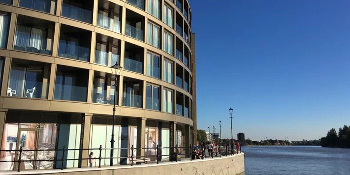 A modern building with large glass windows, surrounded by greenery, showcasing the Riverside Studios logo prominently.