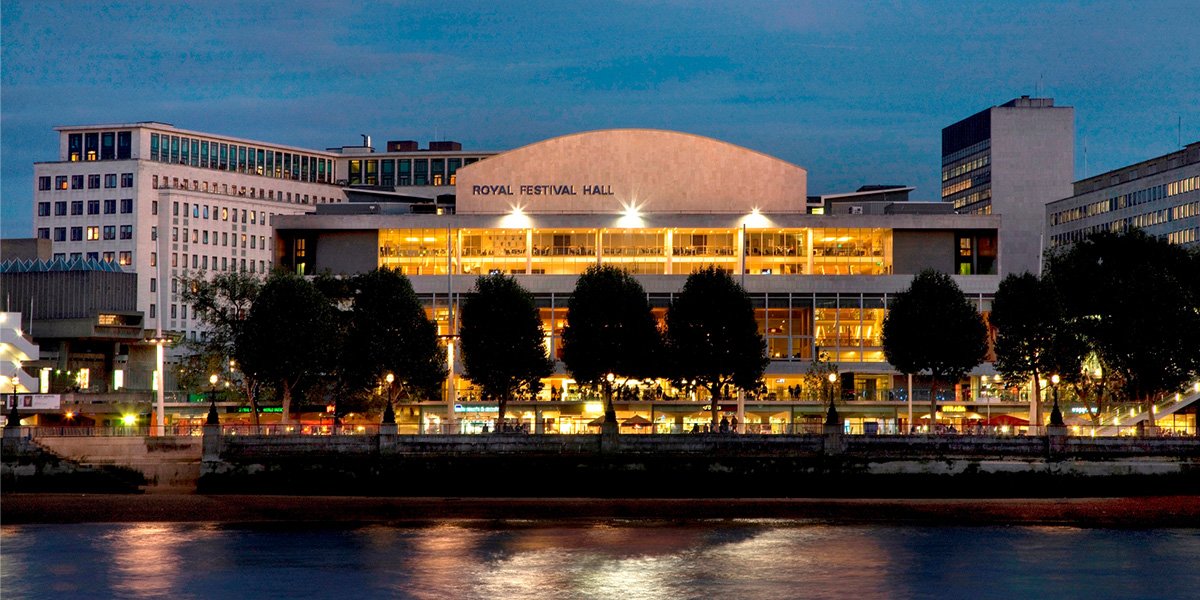View of the Royal Festival Hall across the River Thames, featuring modern architecture and surrounding greenery.
