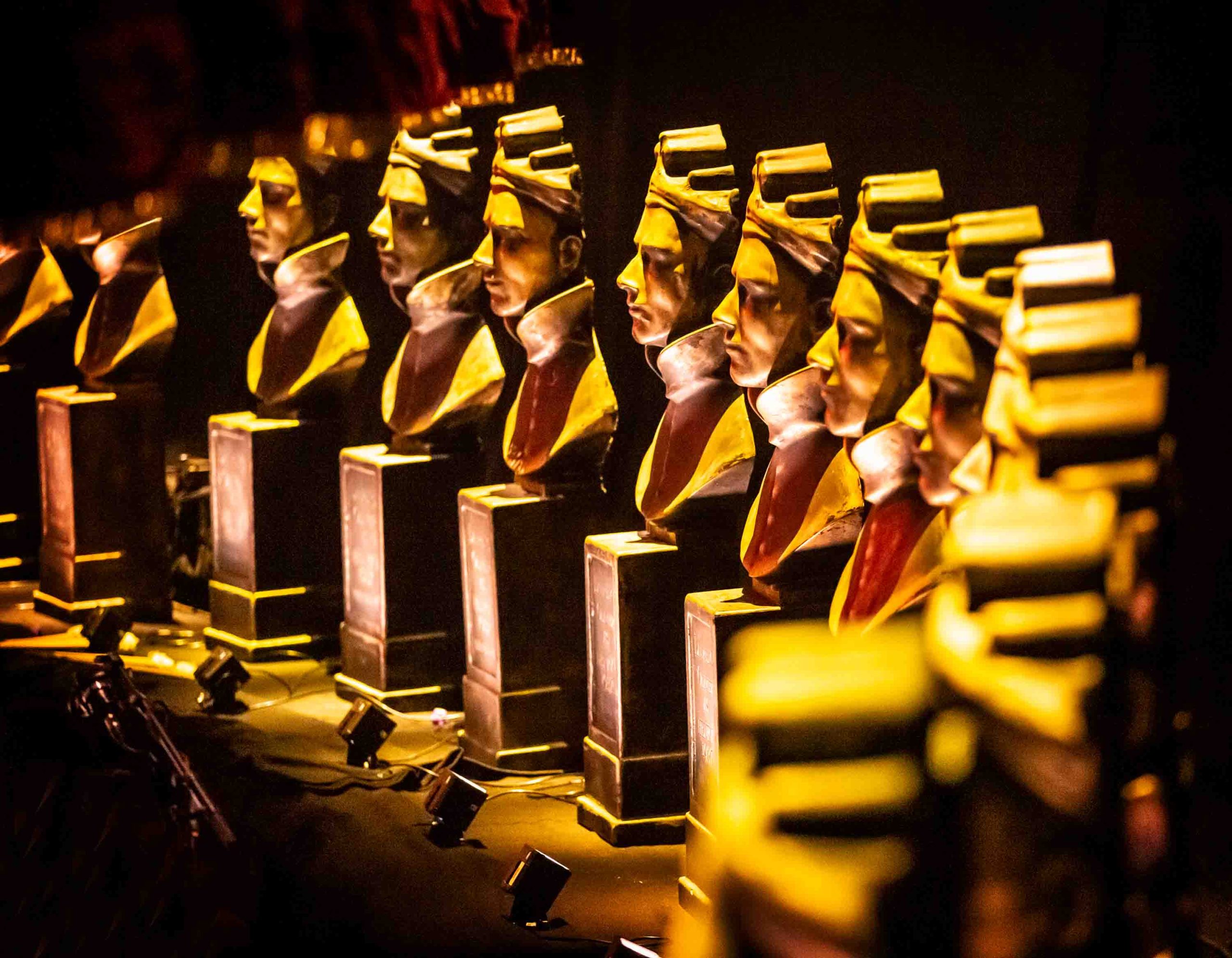 Three Olivier Award statues on a reflective surface, showcasing a gold finish against a blurred background.