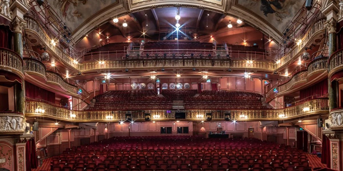 Exterior view of New Wimbledon Theatre, showcasing its ornate architecture and illuminated marquee against a twilight sky.