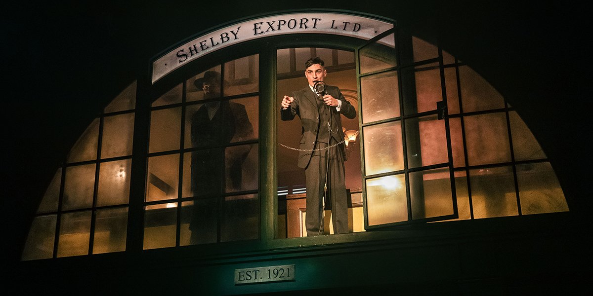 A group of people in military uniforms stands together, smiling, with a backdrop of greenery and trees.