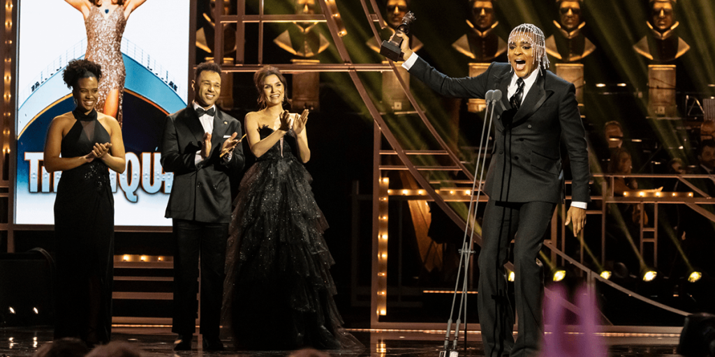 Layton Williams poses confidently on the red carpet, wearing a stylish black suit with a white shirt.