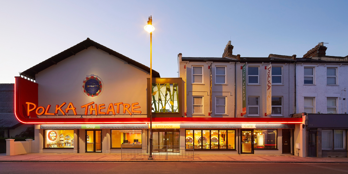 A vibrant theatre stage with colourful decorations, featuring a large backdrop and empty seating in the foreground.